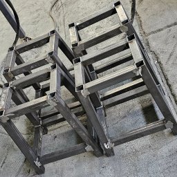 KLARIGA-WELD Maciej Burdziński - Surowe, pospawane metalowe konstrukcje w kształcie prostopadłościanów z kwadratowych profili na szarym betonowym podłożu, widoczne spawy na łączeniach.