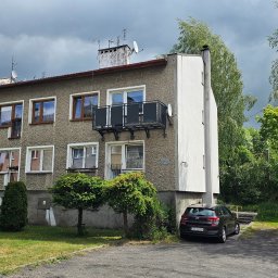 KLARIGA-WELD Maciej Burdziński - Szary blok z balkonem z czarną metalową balustradą, widok z zewnątrz w pochmurny dzień.