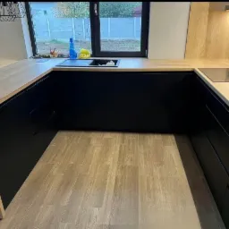 Nowoczesna kuchnia w kształcie litery U z czarnymi frontami szafek i drewnianym blatem, widok na okno z widokiem na ogród.