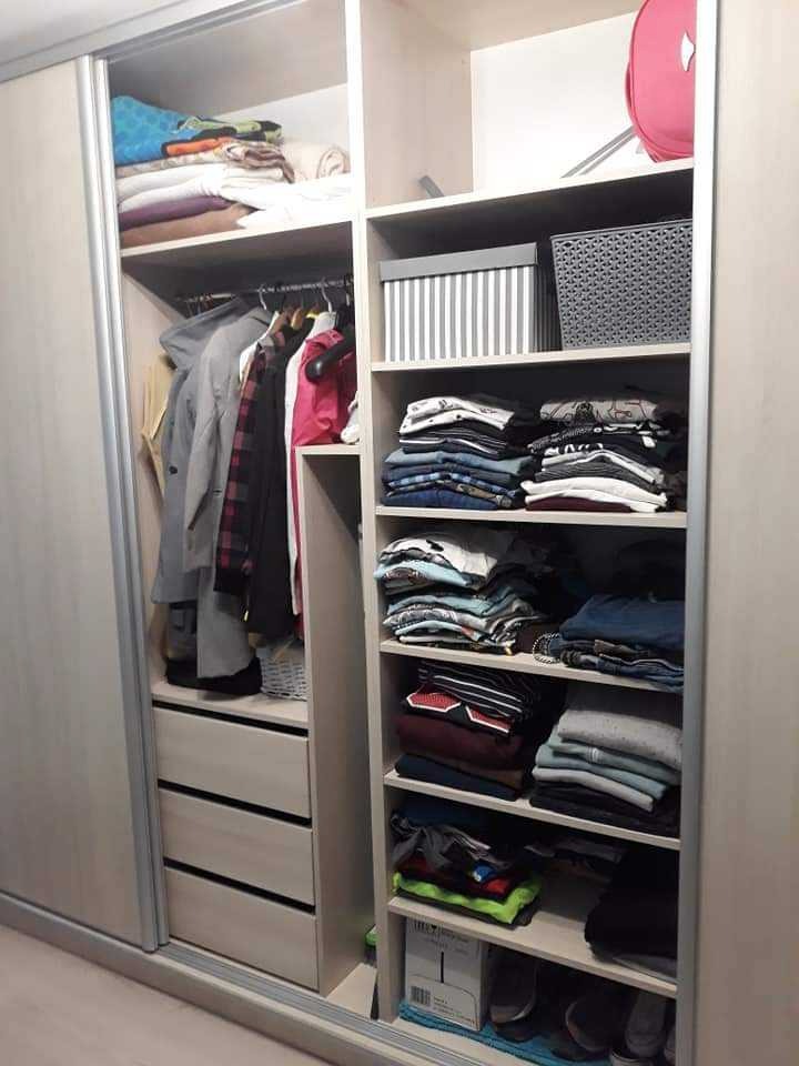 Wnętrze jasnej szafy przesuwnej z szufladami, półkami i drążkiem na ubrania, wypełnione ubraniami, pudełkami i koszami.