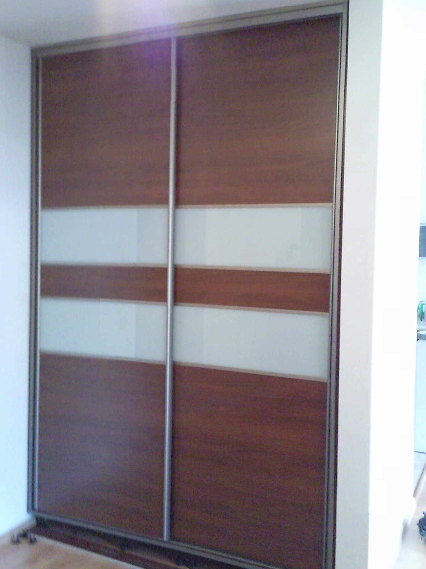 Dwudrzwiowa szafa przesuwna z drewnopodobnymi panelami i poziomymi pasami z mlecznego szkła, zamontowana w mieszkaniu w Częstochowie.