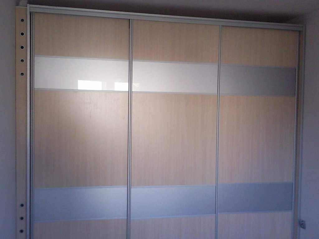 Trzydrzwiowa szafa przesuwna z jasnego drewna z poziomymi pasami szkła matowego i srebrnego.