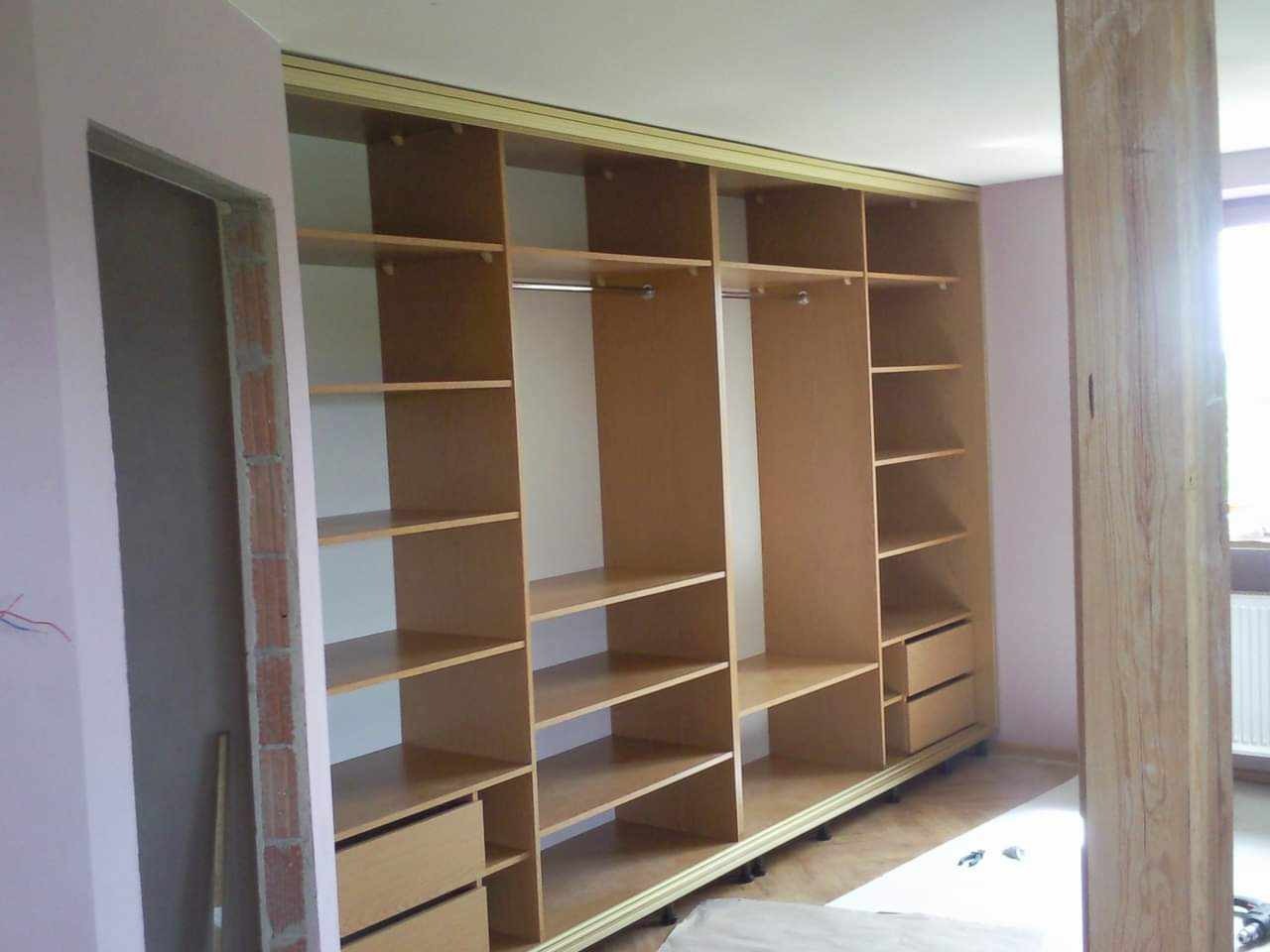 Wnętrze garderoby z jasnego drewna z otwartymi półkami i szufladami, widoczne elementy montażowe w surowym wnętrzu, ściany w trakcie wykańczania.