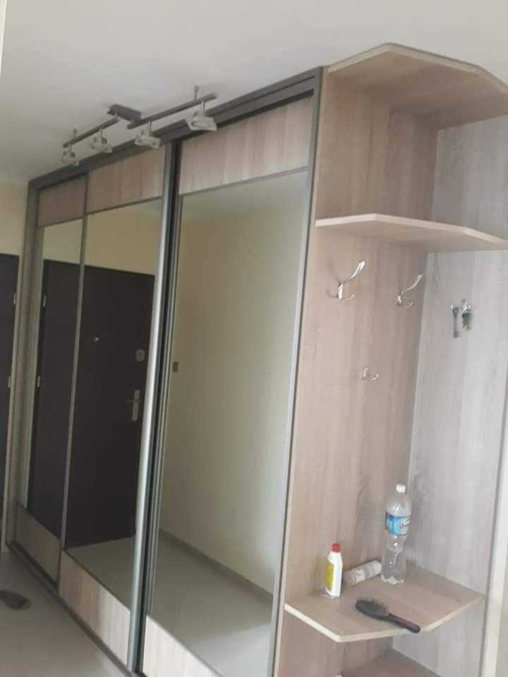 Duża szafa wnękowa z przesuwnymi, lustrzanymi drzwiami i otwartymi półkami z wieszakami, oświetlenie sufitowe, widoczne akcesoria na półce.