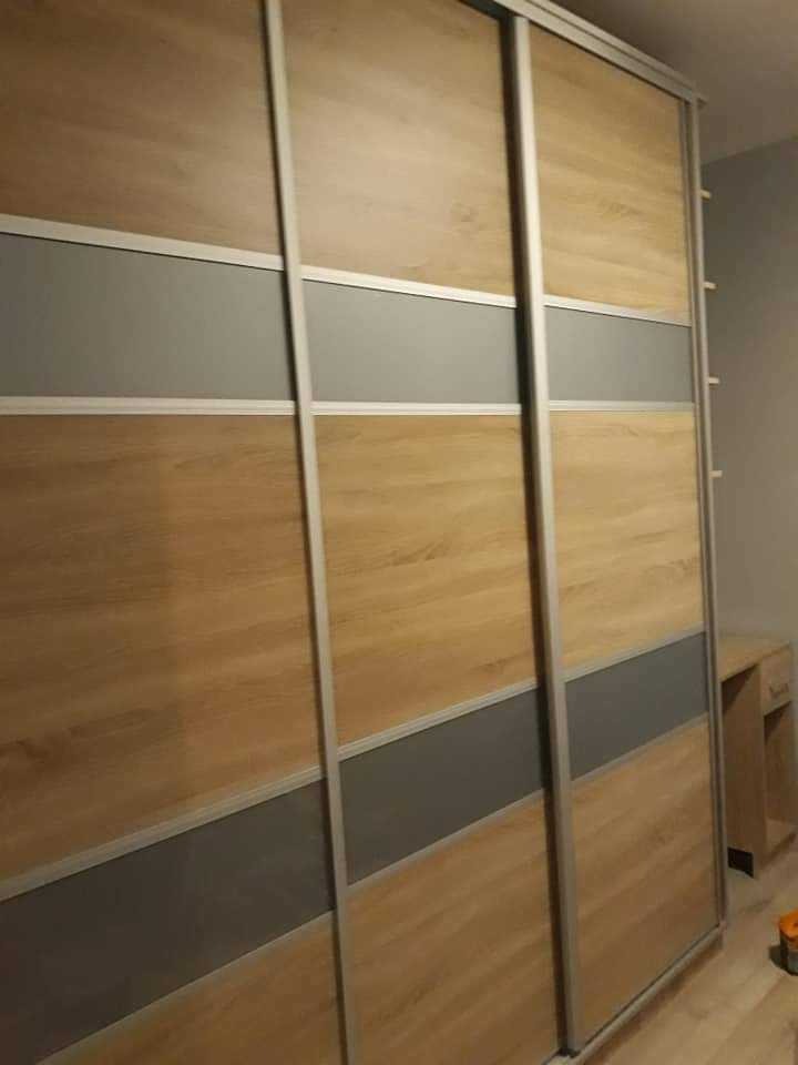 Trzydrzwiowa szafa przesuwna z panelami w odcieniach drewna i szarości, wykończona srebrnymi profilami.