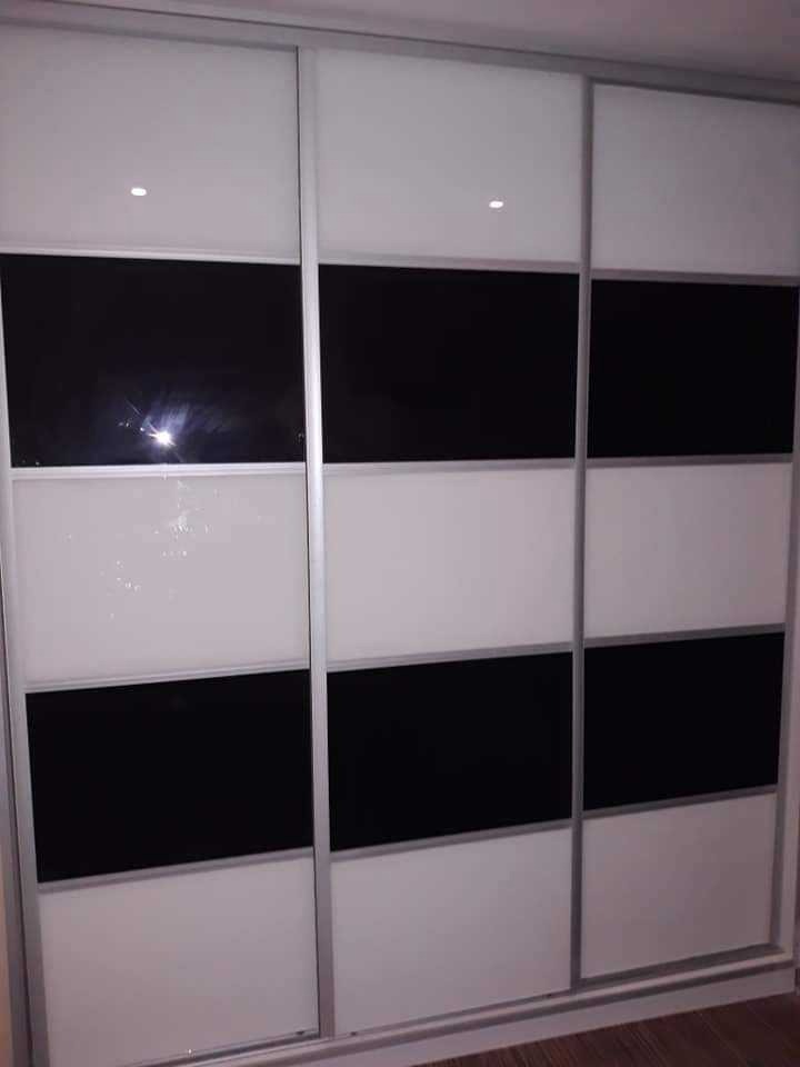 Trzydrzwiowa szafa wnękowa z przesuwnymi drzwiami, z panelami w kolorze białym i czarnym, oświetleniem punktowym w górnej części.