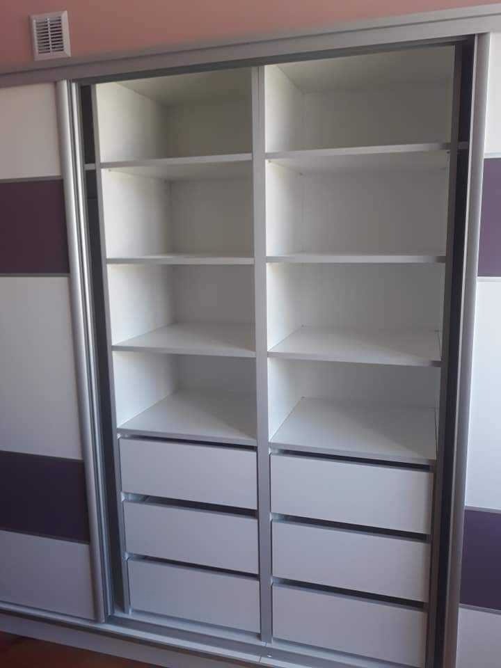 Biała szafa wnękowa z przesuwnymi drzwiami, z szarymi obramowaniami, z półkami i szufladami, z fioletowymi i białymi panelami na drzwiach.