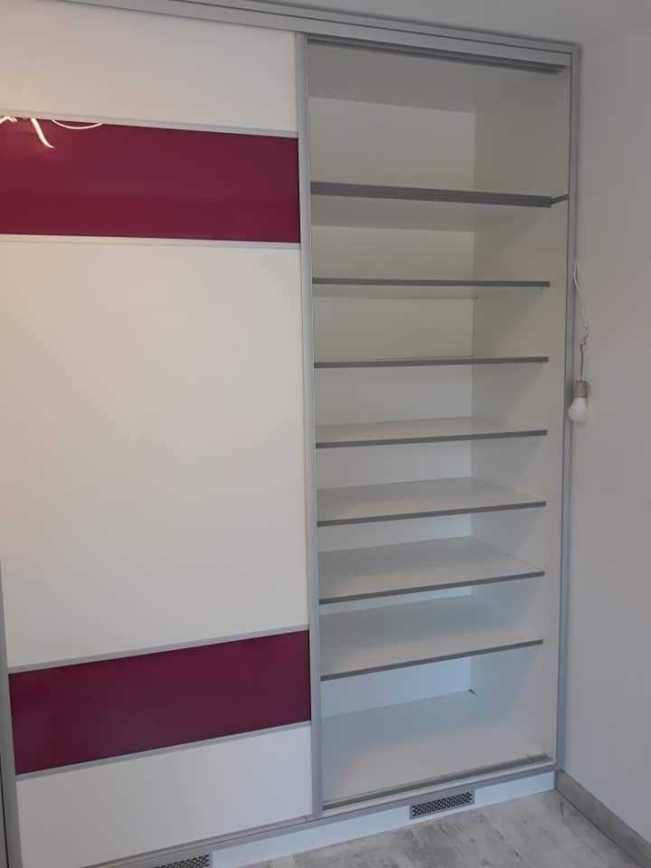 Biało-bordowa szafa przesuwna z otwartą częścią z półkami, widoczna żarówka na kablu, minimalistyczny design.