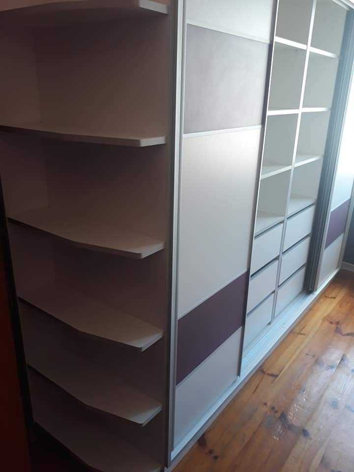 Wnętrze szafy przesuwnej z półkami i szufladami, widoczne drewniane panele dekoracyjne oraz jasne półki, na podłodze parkiet.