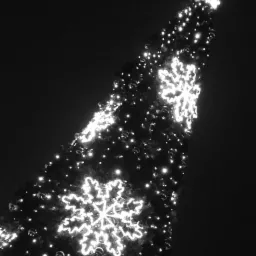 Czarno-białe zdjęcie choinki z dekoracjami w kształcie płatków śniegu i gwiazdą na szczycie, oświetlonej jasnymi lampkami na ciemnym tle nocnego nieba.