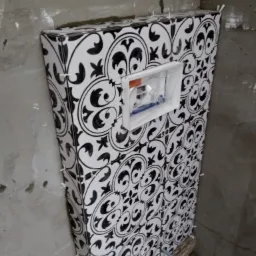 Stelaż podtynkowy WC obłożony wzorzystą, czarno-białą glazurą, widoczne krzyżyki dystansowe i fragment surowej ściany łazienki w trakcie remontu.
