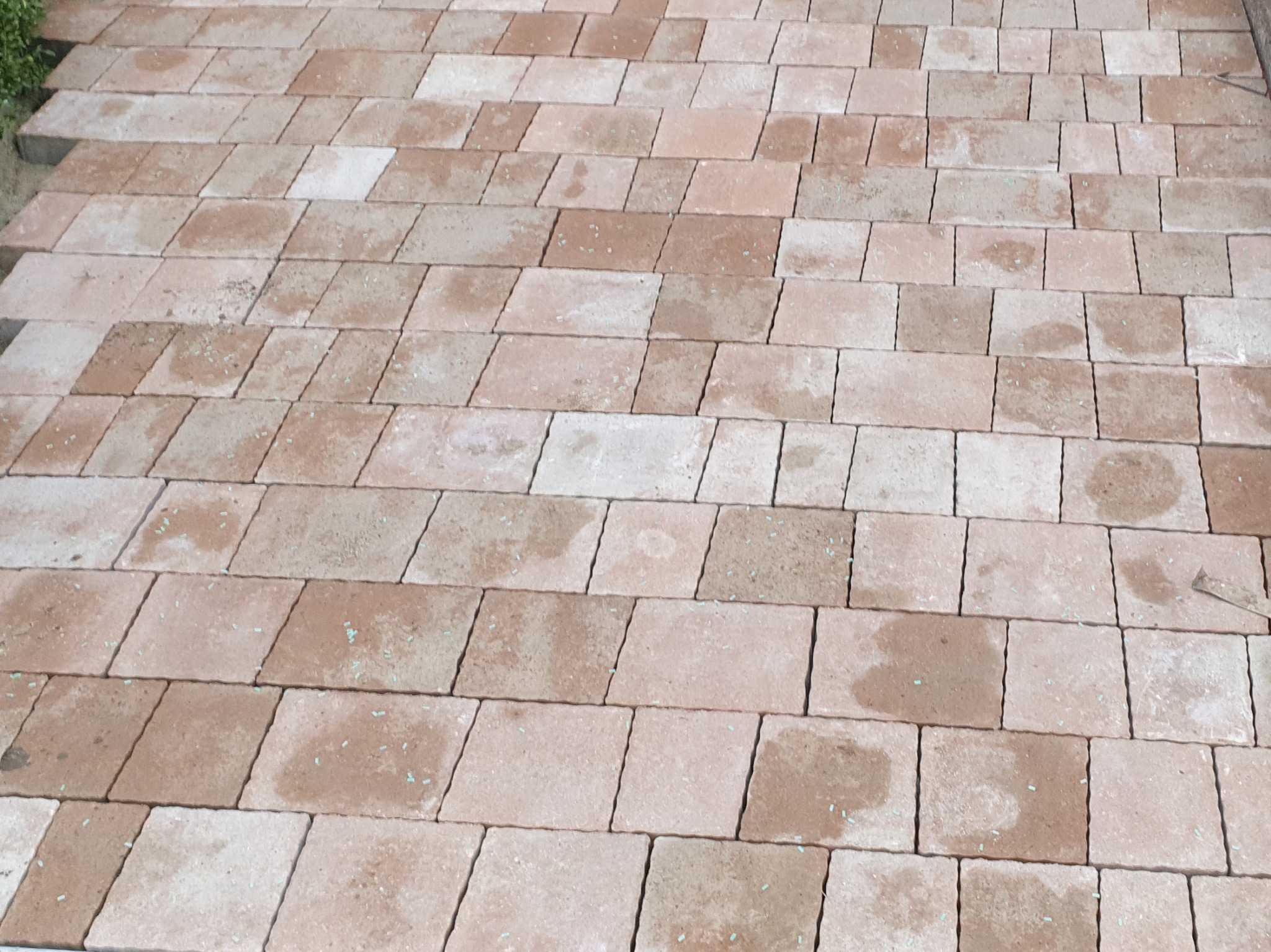 Ułożona nawierzchnia z kostki brukowej w odcieniach beżu i brązu, widoczne drobne zielone elementy w spoinach.
