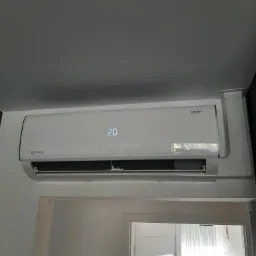 Biała klimatyzacja Rotenso Ukura zamontowana nad futryną drzwi, wyświetlająca temperaturę 20 stopni, widok z dołu.