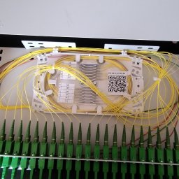 SignalPro - Rozdzielnica światłowodowa Optomer z precyzyjnie ułożonymi, żółtymi kablami. Widoczne zielone złącza i etykiety z numeracją. Estetyczne i uporządkowane okablowanie.