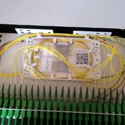 Rozdzielnica światłowodowa Optomer z precyzyjnie ułożonymi, żółtymi kablami. Widoczne zielone złącza i etykiety z numeracją. Estetyczne i uporządkowane okablowanie.