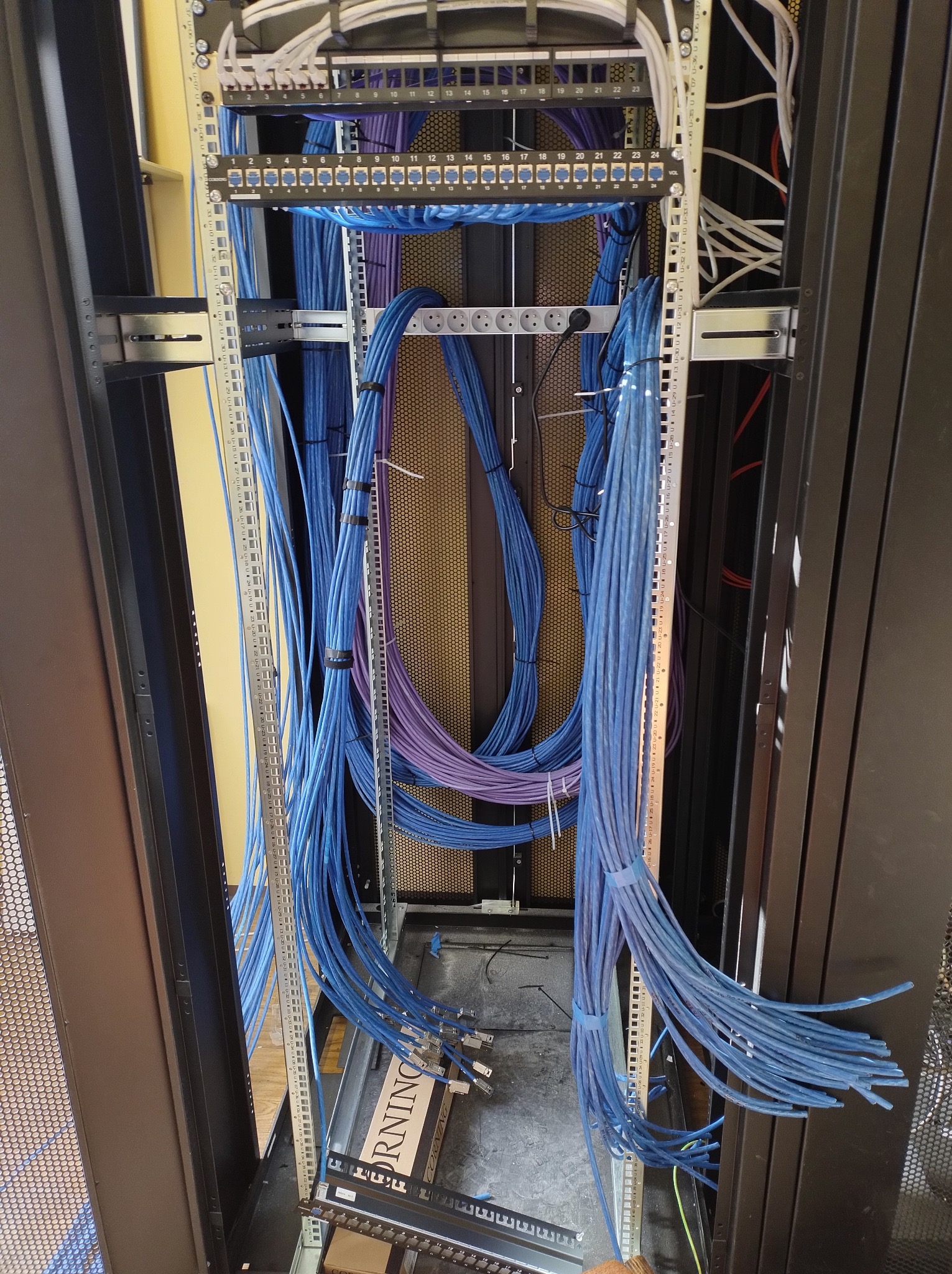 Rozbudowa szafy rack: uporządkowane kable sieciowe (niebieskie i fioletowe) prowadzone wewnątrz metalowej ramy. Widoczne porty i oznaczenia na panelach krosowych.