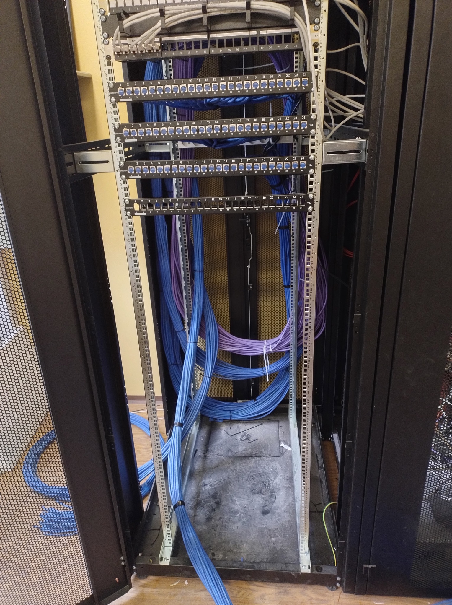 Szafa serwerowa z uporządkowanymi kablami sieciowymi w kolorach niebieskim i fioletowym, widoczne panele krosownicze i oznaczenia portów. Estetyczne ułożenie przewodów.