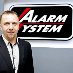 Portret mężczyzny w garniturze na tle logo firmy z branży zabezpieczeń.