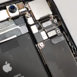 Wnętrze rozłożonego iPhone'a z widoczną baterią, płytą główną i elementami kamery, ukazujące precyzyjną konstrukcję i detale elektroniki.