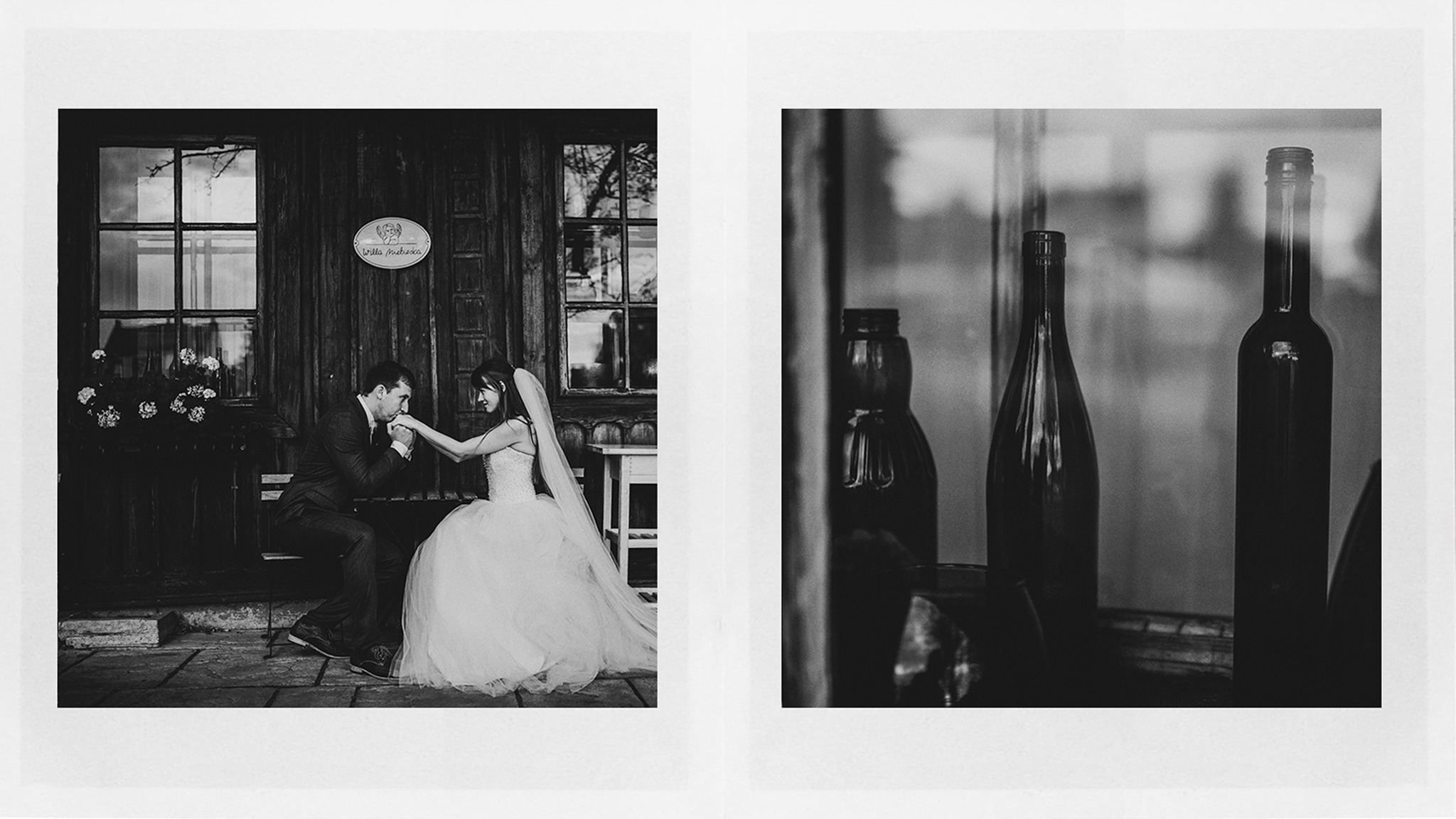 Czarno-białe zdjęcie ślubne: Pan młody całuje dłoń panny młodej siedzącej na ławce przed drewnianym budynkiem z oknami i kwiatami; obok, w odbiciu, widoczne butelki.