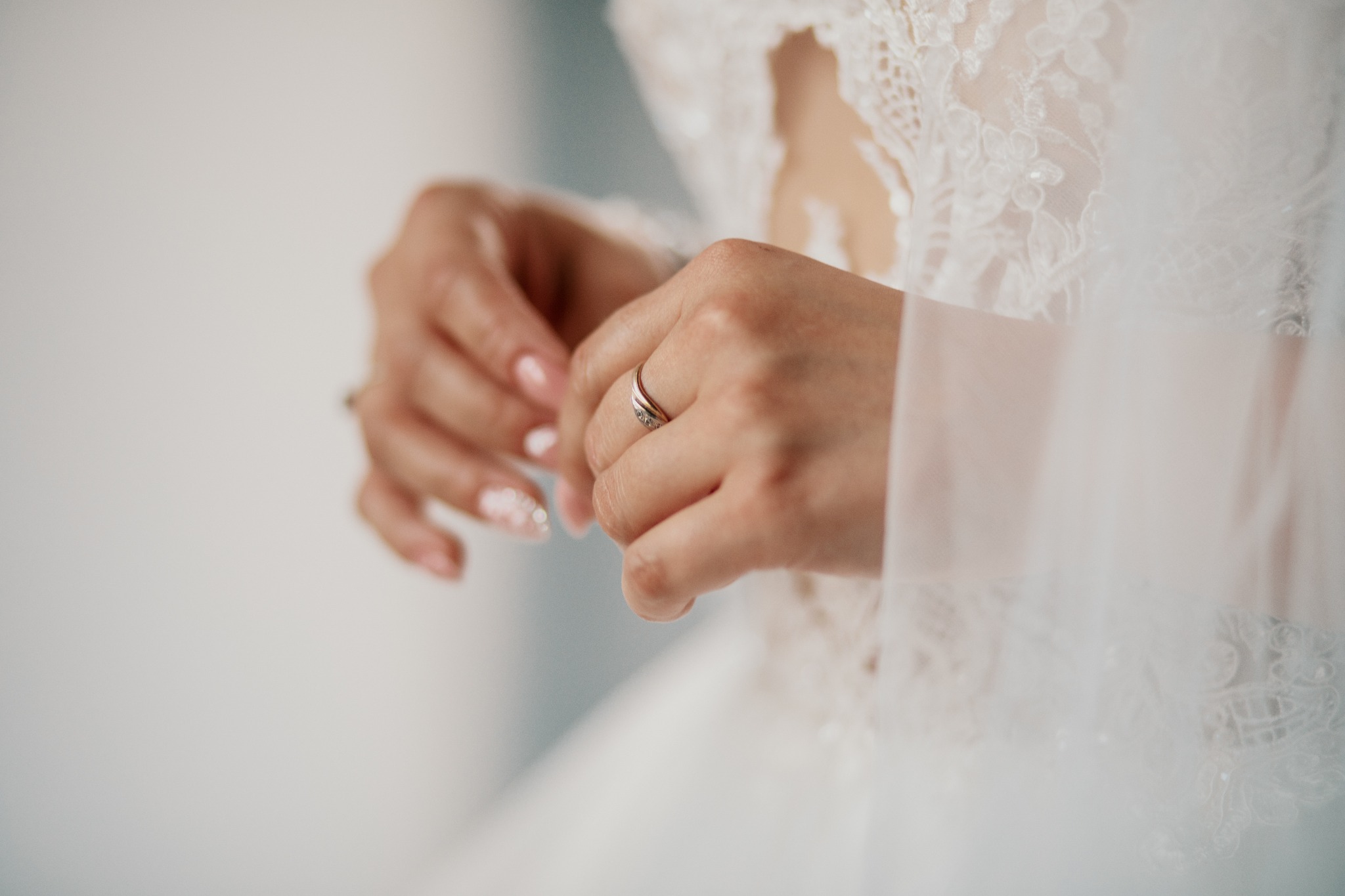 Dłonie panny młodej z pierścionkiem zaręczynowym na tle koronkowej sukni ślubnej.
