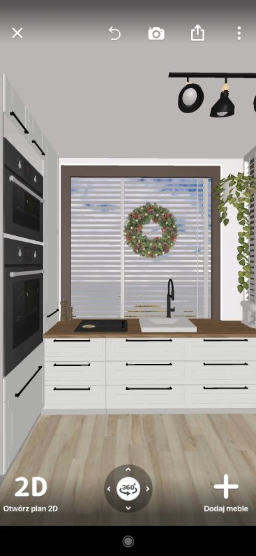 Wizualizacja kuchni z białymi szafkami, drewnianym blatem i czarnymi uchwytami, okno z żaluzjami i świątecznym wieńcem, oświetlenie punktowe na suficie, widok z perspektywy użytkownika aplikacji...