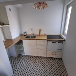 FIRMA USŁUGOWA ADRIAN KALINOWSKI - Jasna kuchnia w bloku: białe szafki z drewnianym blatem, mozaikowa podłoga, okno w skosie. Nowoczesna aranżacja z okapem i płytą indukcyjną.