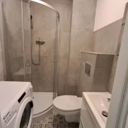 Wykończona łazienka w szarościach: kabina prysznicowa, umywalka z szafką, toaleta i pralka Candy. Wzorzysta podłoga dodaje charakteru.