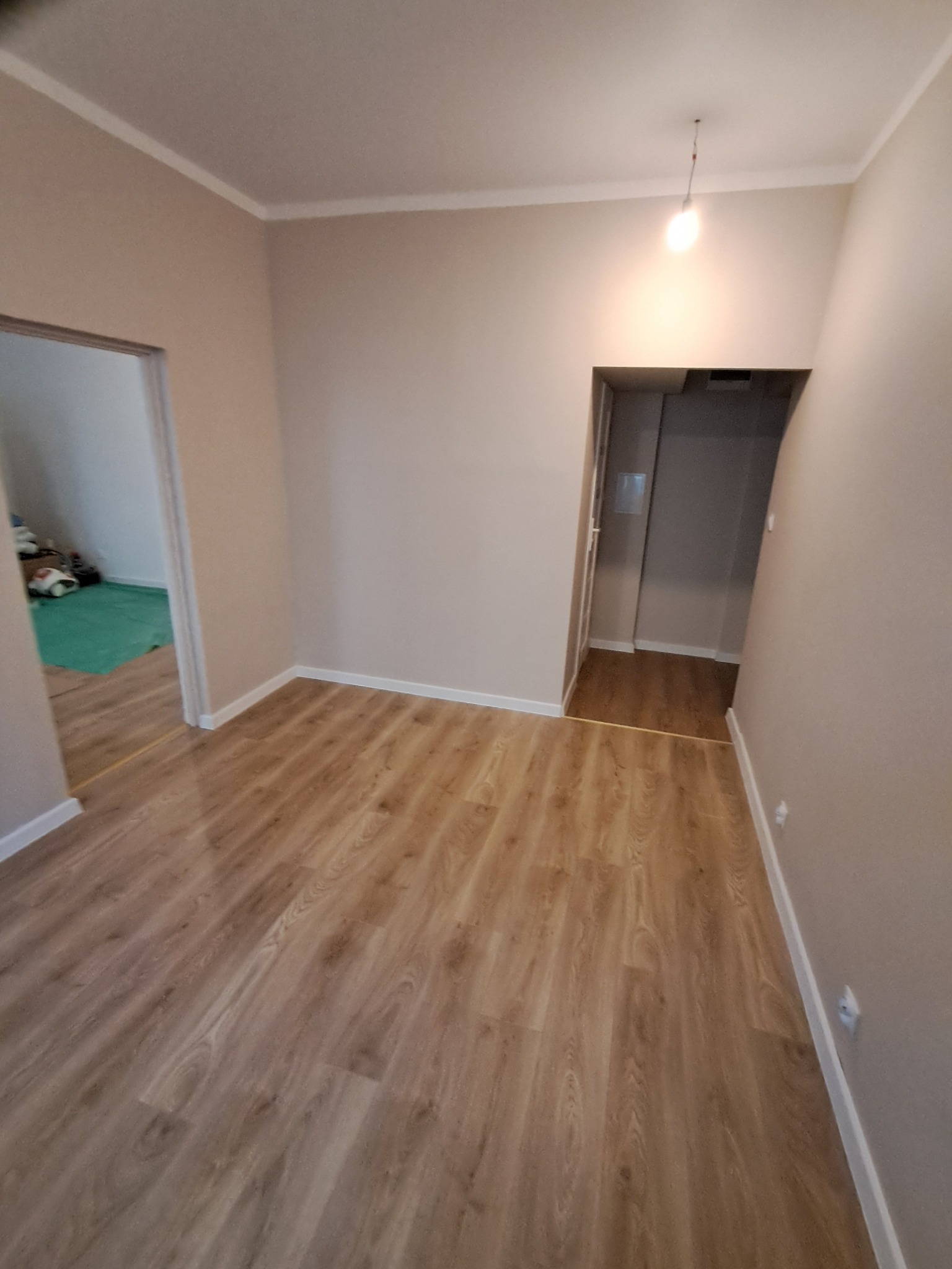 Jasne panele podłogowe w korytarzu po remoncie, widoczne listwy przypodłogowe i wykończenie ścian w neutralnym odcieniu. W tle widoczne otwarte drzwi do innych pomieszczeń.