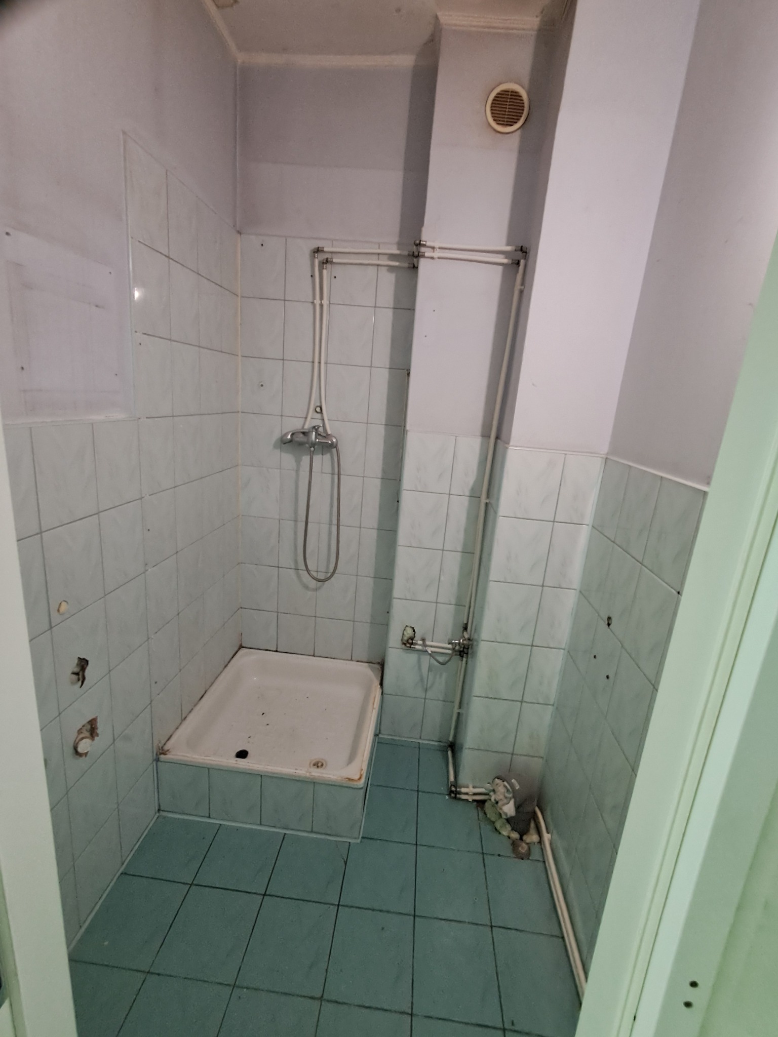 Łazienka przed remontem: stara kabina, białe płytki ścienne z niebieską fugą, niebieska podłoga. Widoczne rury i elementy instalacji. Otwory w ścianach po demontażu.