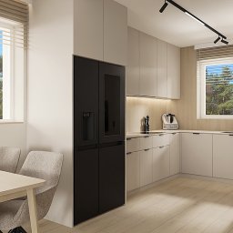 OM Dekor Sylwia Kaczmarek-Bartoszek - Jasna kuchnia z drewnianą podłogą, czarną lodówką i minimalistycznym oświetleniem. Stół z szarymi krzesłami i widokiem na zieleń za oknem.