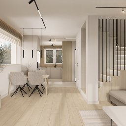 OM Dekor Sylwia Kaczmarek-Bartoszek - Wnętrze domu w neutralnych barwach: drewniana podłoga, schody z czarną balustradą, szara sofa, stół z krzesłami i roślina w doniczce. Minimalistyczny design z nowoczesnym oświetleniem.