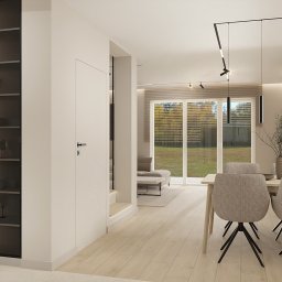 OM Dekor Sylwia Kaczmarek-Bartoszek - Nowoczesne wnętrze: minimalistyczna jadalnia z oświetloną witryną, drewnianym stołem i krzesłami na tle dużego okna z widokiem na ogród. Jasne kolory, proste linie.