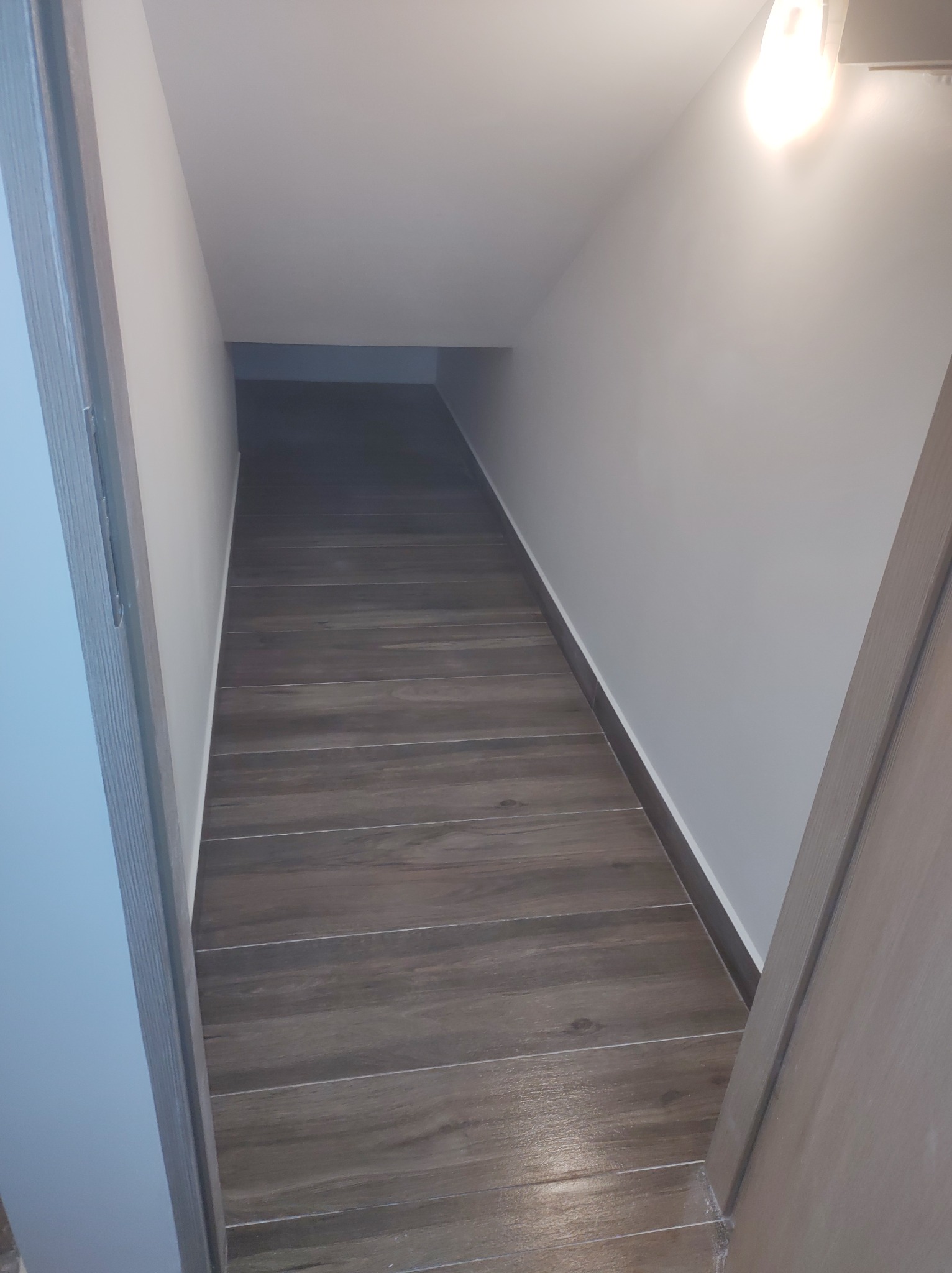 Korytarz z podłogą imitującą drewno, świeżo po położeniu, widoczny fragment futryny drzwi i białe ściany z listwami przypodłogowymi.