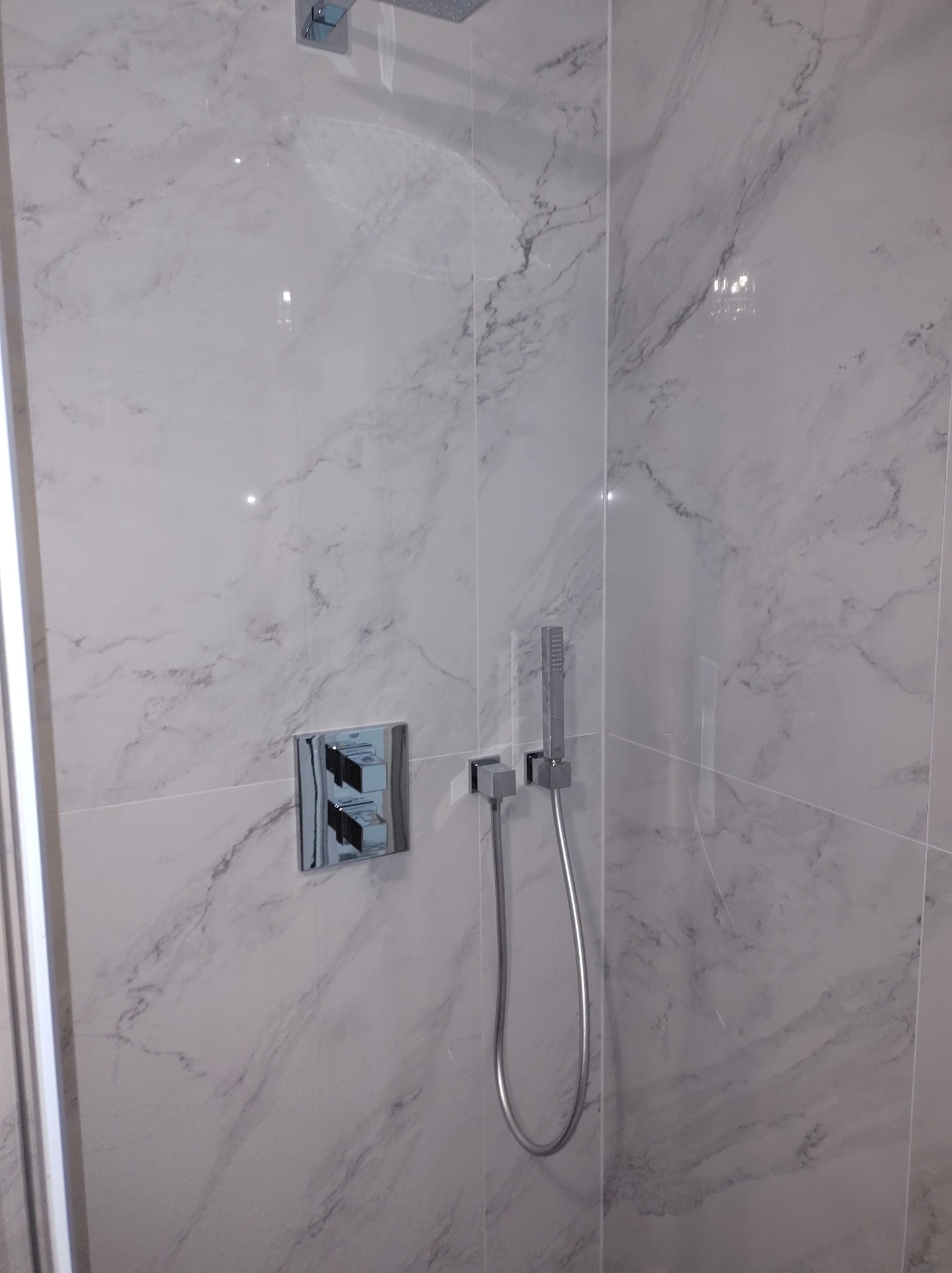 Nowoczesny prysznic z marmurowymi płytkami, chromowaną armaturą i deszczownicą, widok z dołu.