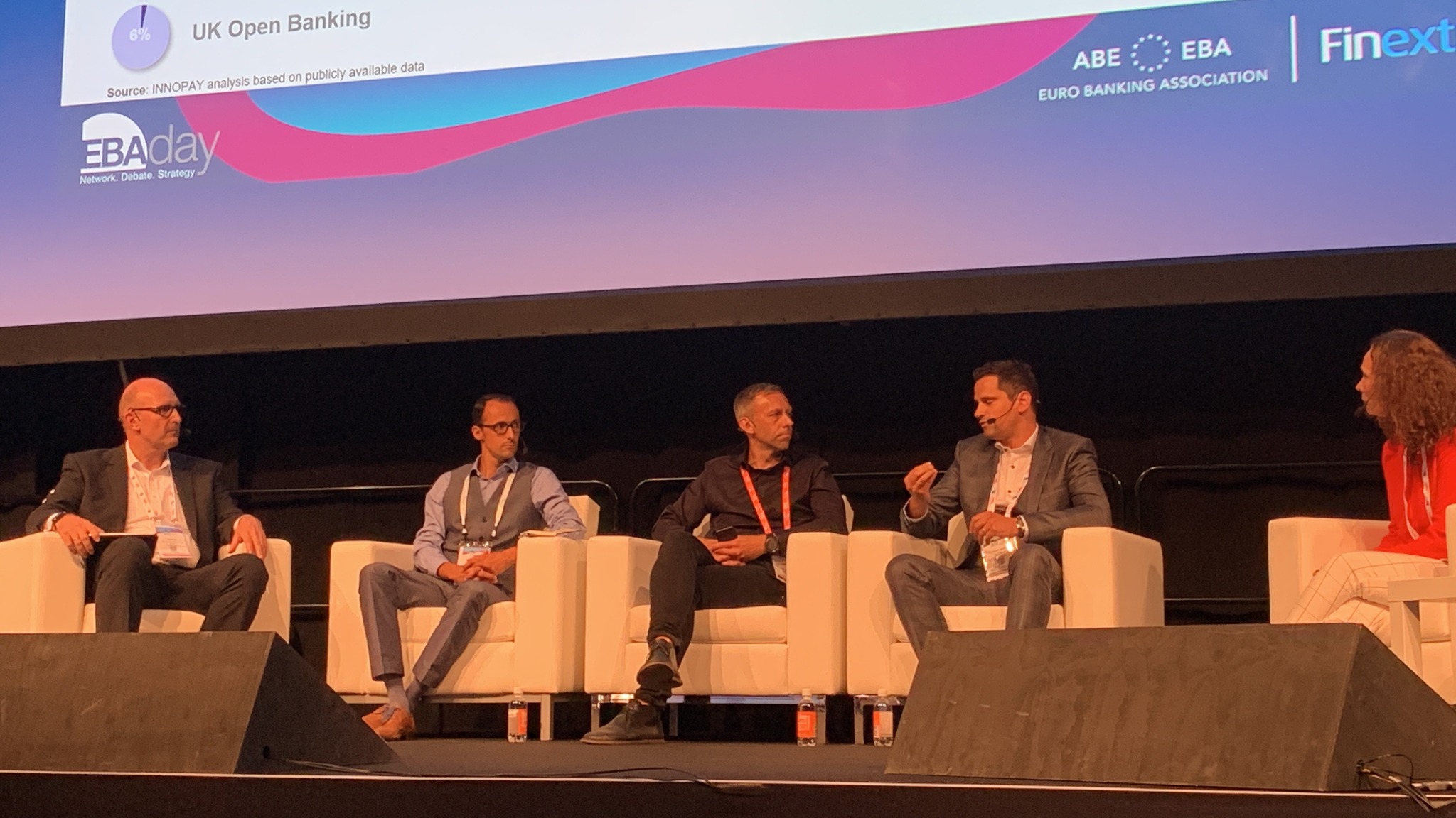 Panel dyskusyjny na scenie z pięcioma osobami siedzącymi w białych fotelach, za nimi ekran z prezentacją o bankowości otwartej i logotypami organizacji finansowych.