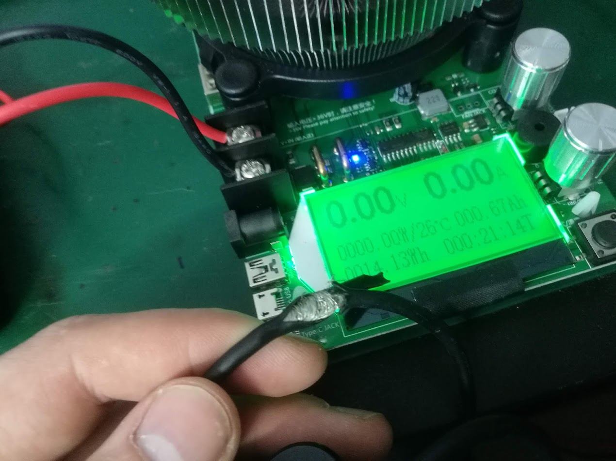 Pomiar napięcia i prądu podczas naprawy kabla USB typu C, z ekranem wyświetlającym wartości 0.00V i 0.00A, z widocznym lutowaniem na kablu i elementami elektronicznymi płyty głównej.