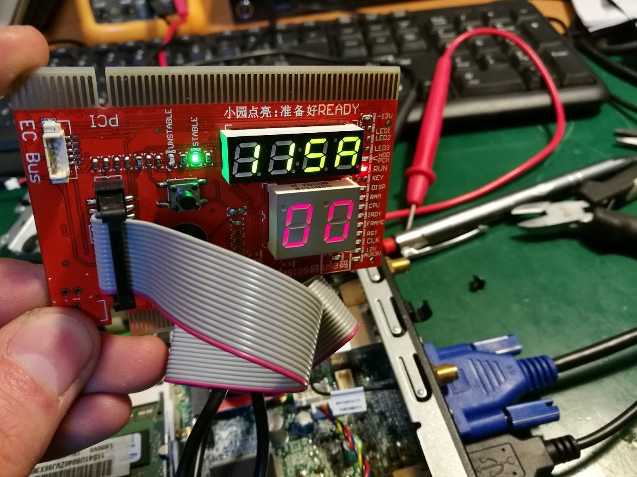 Diagnostyczna karta PCI z wyświetlaczami LED, wskazująca kod błędu, trzymana nad płytą główną komputera podczas testowania, obok miernika i narzędzi.