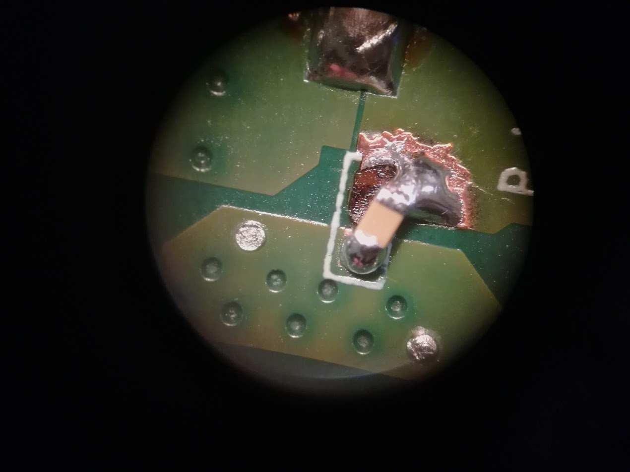 Zbliżenie na naprawiony element elektroniczny na zielonej płytce drukowanej, widoczne punkty lutownicze i ślady topnika, całość sfotografowana pod dużym powiększeniem.