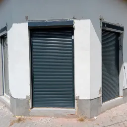 Montaż szarych rolet na elewacji budynku, widoczne ślady prac wykończeniowych, pianka montażowa i przewody elektryczne na zewnątrz.