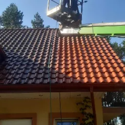 Częściowo umyty dach z czerwonej dachówki w Pokrzywnicy, widoczna różnica w kolorze między czystą a brudną powierzchnią, platforma robocza na wysięgniku.