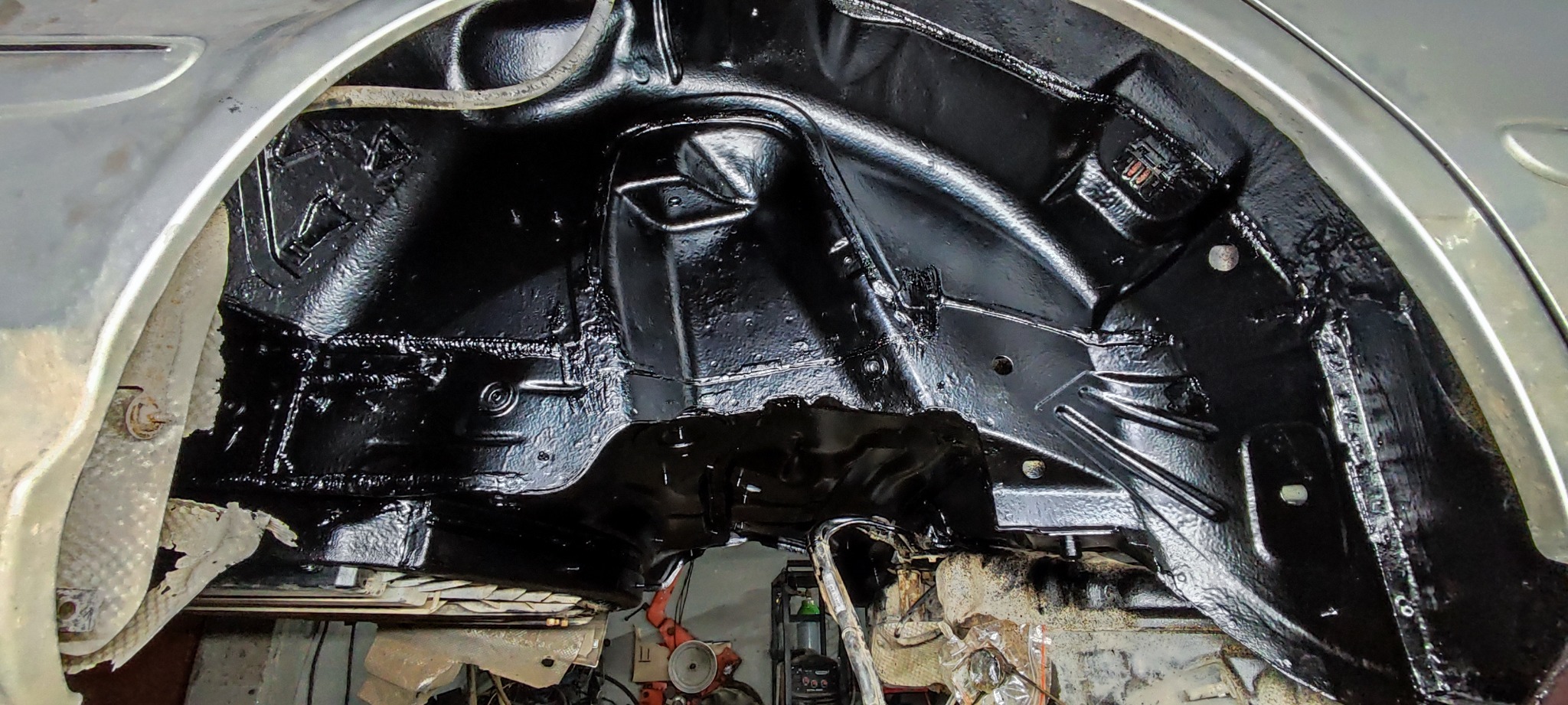Wnętrze nadkola samochodu po zabezpieczeniu antykorozyjnym, widoczna świeża, czarna powłoka ochronna.