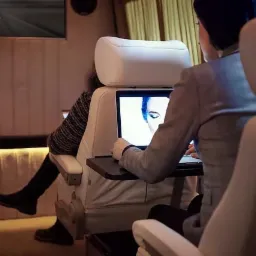 Wnętrze luksusowego busa z dwoma pasażerami, jeden pracuje na laptopie zamontowanym na stoliku przy fotelu, drugi siedzi zrelaksowany, oświetlenie LED w tle.