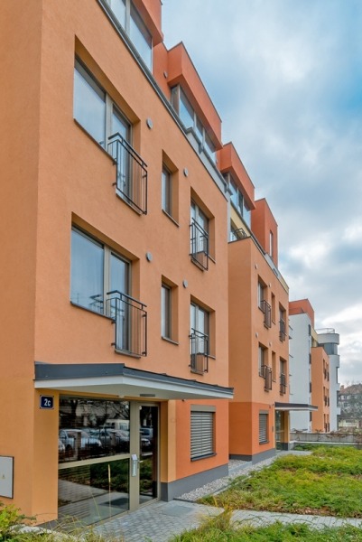 Nowoczesny budynek mieszkalny z pomarańczową elewacją, aluminiowymi oknami i przeszklonym wejściem, widok z zewnątrz w pochmurny dzień.