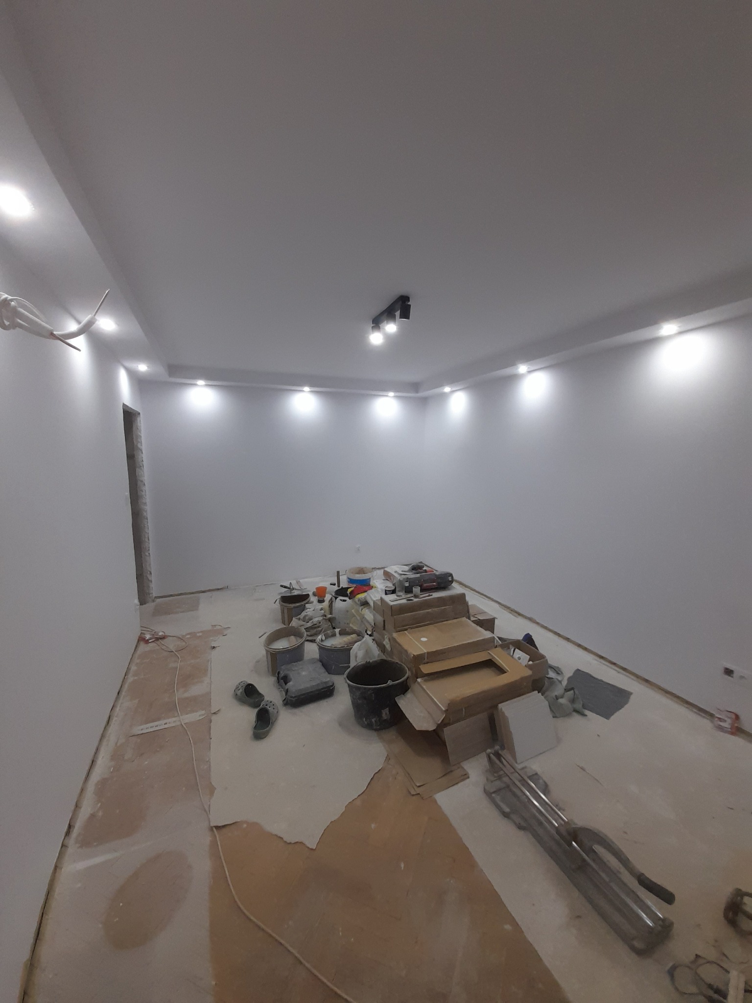 Pokój po szpachlowaniu i malowaniu na biało, widoczne narzędzia i materiały budowlane, sufit z oświetleniem punktowym, przygotowany do dalszych prac wykończeniowych.