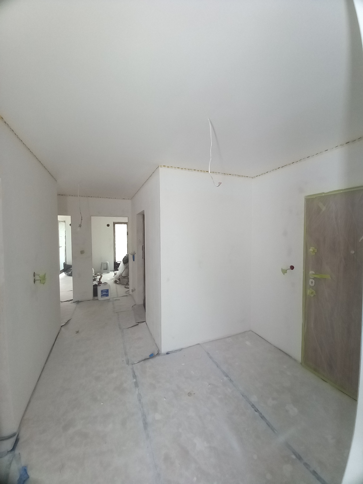 Białe ściany w mieszkaniu po szpachlowaniu, zabezpieczone podłogi folią malarską, widoczne kable wystające z sufitu, przygotowanie do malowania.
