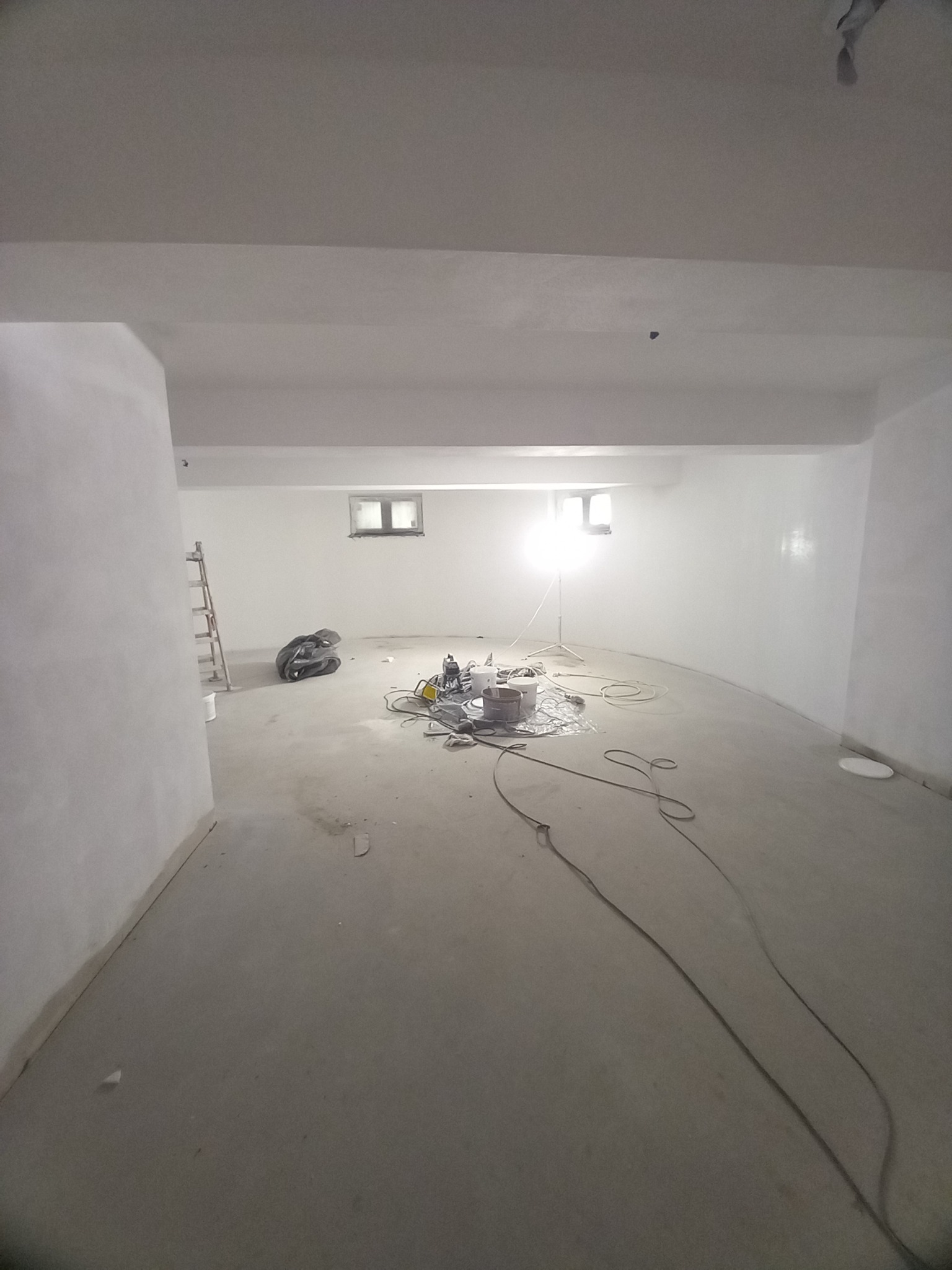 Wnętrze w trakcie prac wykończeniowych: białe, świeżo pomalowane ściany, rozstawione narzędzia i lampa oświetlająca przestrzeń, przygotowane do dalszych działań.