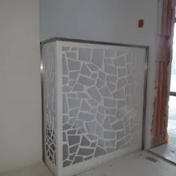 Ażurowa ścianka działowa z białego tworzywa i metalowym obramowaniem w surowym wnętrzu, widoczne ślady prac wykończeniowych.