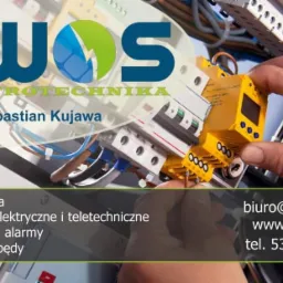 Grafika reklamowa firmy elektrycznej EWOS, przedstawiająca dłoń instalatora pracującego przy żółtym module elektrycznym, widoczne również bezpieczniki i przewody. W tle logo firmy oraz dane...