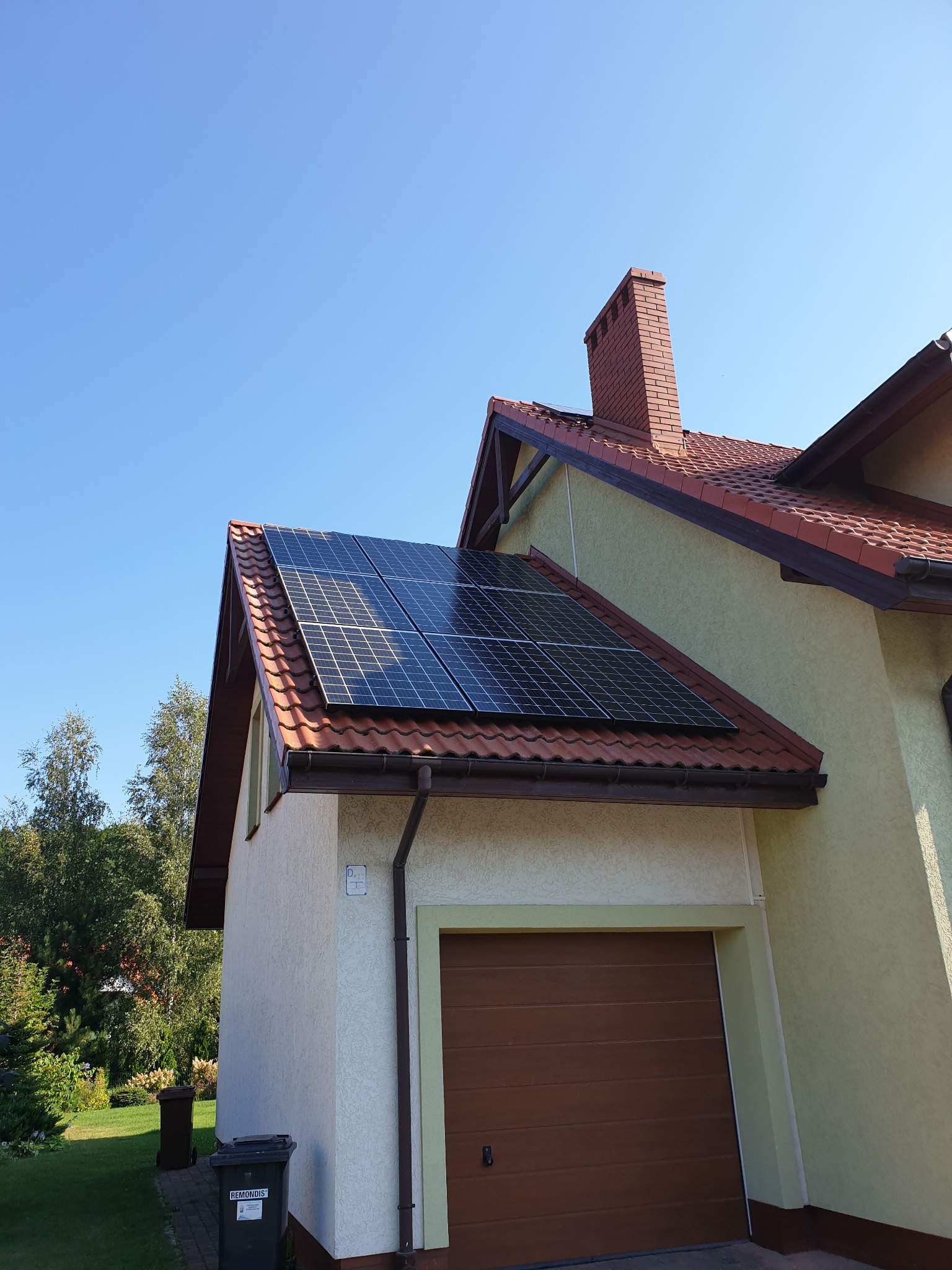 Panele słoneczne na dachu domu jednorodzinnego z czerwoną dachówką, widok z dołu na błękitne niebo.